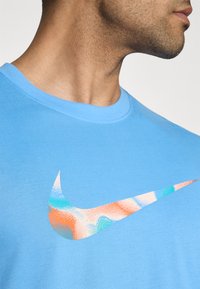 Camiseta de algodón azul claro con un logo de Nike multicolor con efecto de degradado texturizado. Diseño de cuello minimalista, mangas cortas.