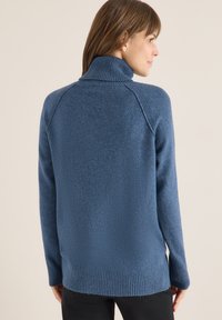 Niebieski sweter robiony na drutach z wysokim kołnierzem, ściągaczami przy mankietach i u dołu; miękka tekstura i luźny krój; prosty design bez wzorów.