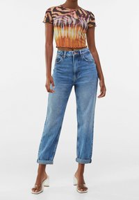 Zkrácený, průhledný top s oranžovým, růžovým a černým tygřím pruhovaným vzorem. Vysoce pasové, světle modré, mírně opotřebované džíny s ohrnutými nohavicemi.