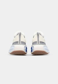 Nike running shoes with a soft white upper, grey accents, a textured brown sole, and a blue logo detail on the heel. Designed for comfort.