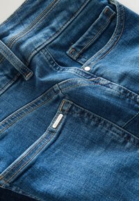 Zbliżenie na niebieskie dżinsy z denimu, pokazujące przednie kieszenie, szlufki na pasek i detale przeszyć.