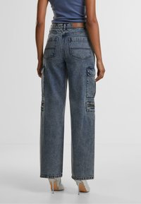 Wide-leg denim cargo pants in light blue with multiple pockets, a textured finish, and a high waist. Includes a leather label at the back.