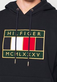 Felpa navy con cappuccio regolabile, caratterizzata da un logo ricamato multicolore. Dettagli degni di nota includono accenti dorati e un design a patch rettangolare.