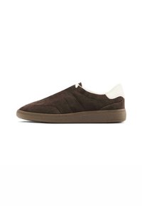 Scarpe slip-on in suede marrone con punta leggermente arrotondata, suola testurizzata e accenti bianchi a contrasto sul tallone. Fodera interna liscia.