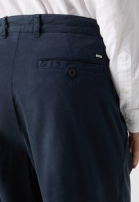 Ναυτικό μπλε βαμβακερό παντελόνι με κουμπωτή πίσω τσέπη και πάτσα με το λογότυπο "BOSS". Λείο υφασμά, κομψή εφαρμογή και τρύπες για ζώνη.