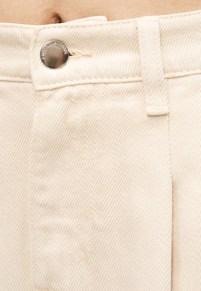 Μπεζ denim παντελόνια με φερμουάρ, διαθέτουν κλείσιμο με ασημένιο κουμπί και υφή επιφάνειας. Η ραφή είναι ορατή κατά μήκος των ραφών.