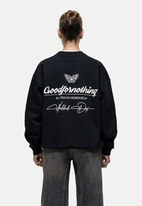 Felpa nera in cotone con spalle scese, con una grafica di una farfalla bianca e il testo "Goodfornothing" sul retro. Vestibilità rilassata.