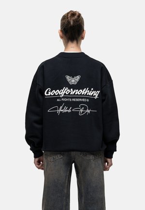 Felpa nera in cotone con spalle scese, con una grafica di una farfalla bianca e il testo "Goodfornothing" sul retro. Vestibilità rilassata.