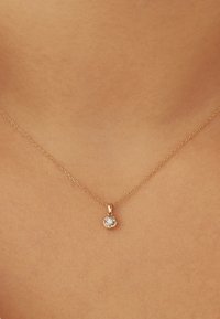 Delicate gold chain necklace with a small round diamond pendant worn on bare skin at the center of the collarbone.