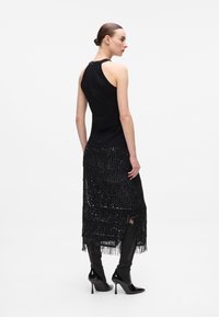 Black sleeveless top with a smooth texture, paired with a fringed black sequin skirt. The outfit is complemented by glossy black heels.