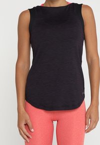 Musta ilmanhihainen urheilu paita, jossa on teksturoitu kangas ja mustat olkaimet, yhdistettynä kirkkaan pinkkeihin legginsseihin. Kaareva helma.