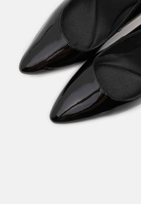 Ballerines en cuir verni noir avec un bout pointu et des côtés ouverts. Présentent une texture lisse et des semelles intérieures rembourrées pour le confort.