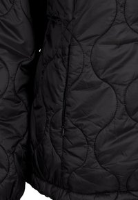 Giacca nera trapuntata con un motivo a zig zag circolare, tasche laterali con zip e orlo elasticizzato, realizzata in tessuto leggero.