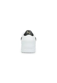 Sneaker bianca con dettagli neri, tomaia in pelle testurizzata, collare imbottito e una suola bianca spessa. Presenta un logo dorato sul tallone.