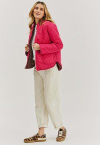 Jasnoróżowa pikowana kurtka z podszewką w panterkę, noszona na białej bluzce i kremowych spodniach, uzupełniona o trampki w panterkę.