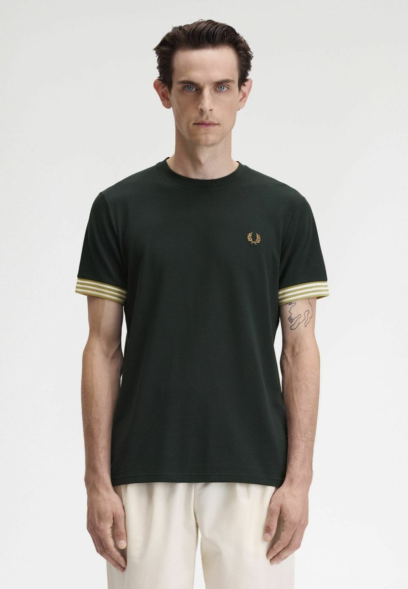 T-shirt in cotone verde scuro con maniche a righe gialle e bianche, colletto a girocollo e un piccolo logo dorato sul petto. Texture liscia.