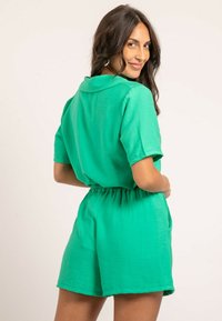Jupe-short verte avec un col, des manches courtes, une taille élastique et une texture lisse. Présente une coupe décontractée et des poches latérales.