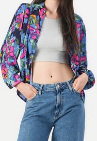 Blouse légère à motifs floraux en marine, rose et vert, associée à un top gris court et à un jean en denim bleu taille haute.