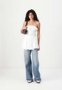 Λευκή τοπ χωρίς straps με συλλεγμένη υφή και ρέουσα φούστα; συνδυασμένο με ανοιχτό μπλε φαρδύ τζιν. Αξεσουάρ με μια μικρή γκρι τσάντα χειρός.