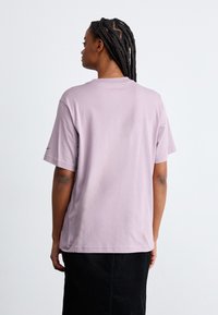 Camiseta de algodón lila con mangas cortas y un corte relajado. La parte posterior presenta un escote redondeado y detalles de costura mínimos.