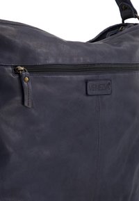 Marineblauwe leren handtas met een zachte textuur, voorzien van een ritszak en een merkembleem. Subtiele accenten zijn onder andere messing hardware en stiksels.