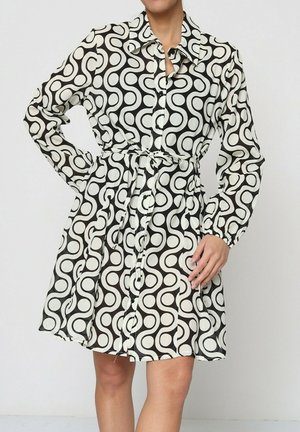 Robe chemise à manches longues avec un motif circulaire noir et blanc. Elle présente un col, une fermeture à boutons sur le devant et une ceinture à la taille.