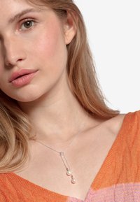 Sølv halskæde med tre perler; delikat kæde; to perler hænger fra en central forbindelse; båret af en person i en levende orange top.
