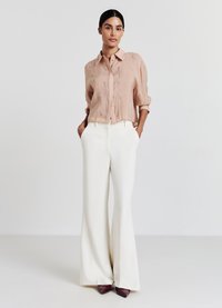 Blusa rosa chiaro con chiusura a bottoni e ricami sottili, abbinata a pantaloni bianchi a vita alta e zeppe punta a punta color bordeaux.