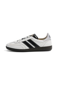 Baskets basses blanches avec des rayures noires, une semelle noire et le logo "GOLA" sur le talon et la languette, vues de profil.