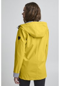 Yellow waterproof jacket with a hood, featuring a black logo patch on the shoulder and a striped inner lining. Long sleeves with striped cuffs.