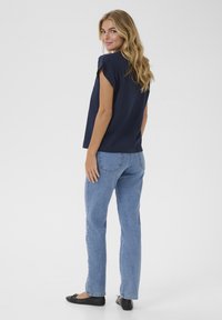 Top de manga corta azul marino con un corte relajado, combinado con jeans de pierna recta azul claro y bailarinas negras. Tejido suave con un detalle mínimo.