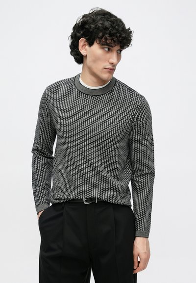 Džemperis ar teksturētu melnu un baltu rakstu, apaļu izgriezumu un garām piedurknēm. Kombinēts ar melnām biksēm.