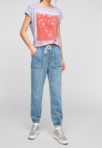 Camiseta de color púrpura claro con un gráfico floral rojo y texto, combinada con joggers de mezclilla azul claro sueltos que tienen puños elásticos y bolsillos.