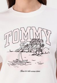 Balta medvilninė marškinėlių su grafiniu dizainu, kuriame užrašyta „TOMMY Jeans“, palmių medžiai ir buriavimo laivas juodu ir rožiniu rašalu.