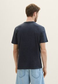 Mørkeblå bomulds t-shirt med korte ærmer, rund hals og synlige syninger. Båret med lyseblå denimshorts.