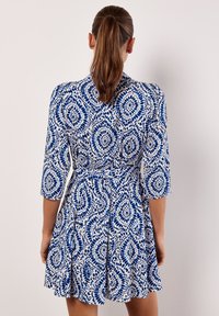 Abito a maniche corte con corpetto aderente e gonna svasata, caratterizzato da un motivo circolare blu e bianco su tessuto leggero.