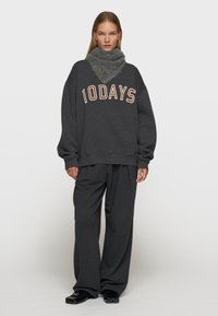 Felpa oversized grigio scuro con la scritta "10DAYS" in colore contrastante, abbinata a pantaloni a gamba larga coordinati e a un caldo collo in tessuto morbido.