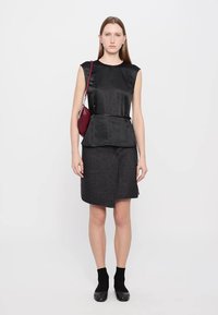 Čierny saténový top s krátkymi rukávmi, peplum pás; tmavosivá sukňa s diagonálnym strihom a detailom gombíka. Čierne členkové ponožky a baleríny.