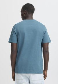 Kortærmet T-shirt med rund hals i dæmpet blå bomuld, som har en afslappet pasform og enkelt design. Bagsiden viser syningsdetaljer og tekstur.