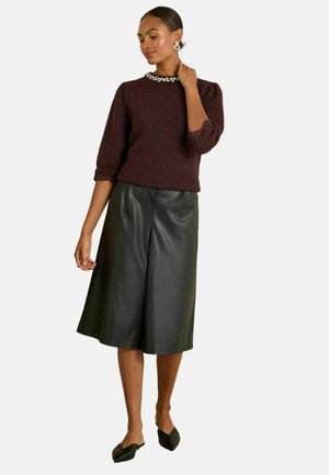 Maroon knitted sweater with a beaded neckline, paired with A-line black leather culotte shorts. Model wears black slip-on shoes.