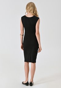 Robe noire ajustée avec des manches courtes, fermeture éclair au dos et une fente à l'ourlet. Tissu lisse avec une silhouette élégante.