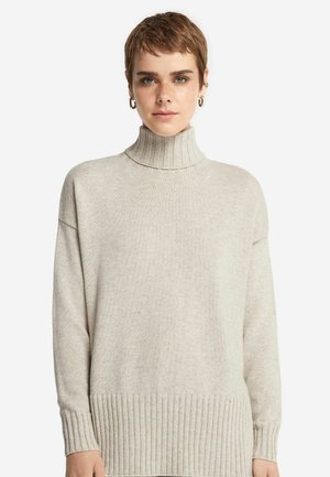 Beige polotröja gjord av mjukt stickat tyg. Har en ribbad krage och nederkant, lös passform med sänkta axlar och subtil textur.