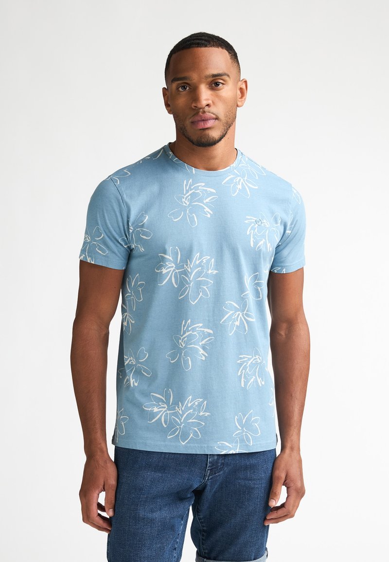 Hellblaues kurzärmeliges T-Shirt mit weißen Blumenmustern, Rundhalsausschnitt und weichem Baumwollstoff. Kombiniert mit dunklen Denim-Jeans.