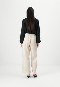 Black long-sleeve top paired with cream, textured, wide-leg pants. The outfit is completed with black heeled mules.