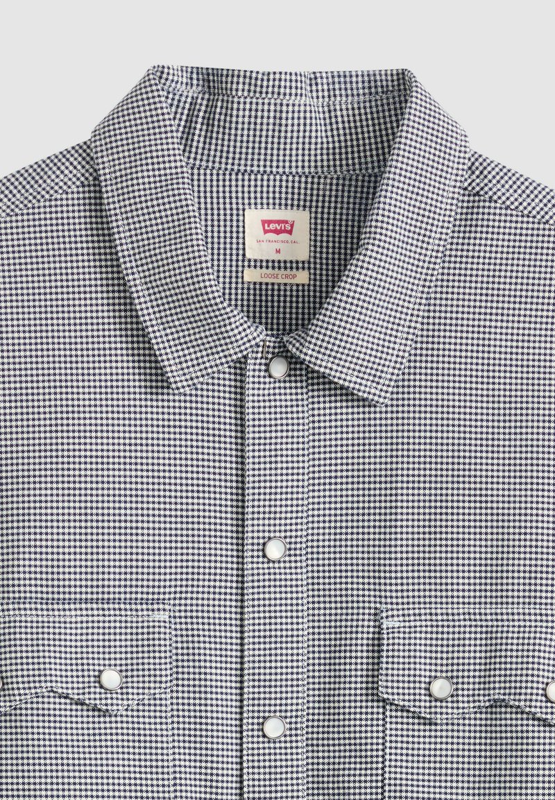 Camicia a quadretti piccoli in bianco e nero con collo appuntito, due tasche frontali con bottoni e etichetta Levi's all'interno del collo.