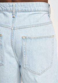 Lyseblå denimjeans med midjehøyde, to baklommer og kontrasterende sømmer langs sømmene. Glatt tekstur.