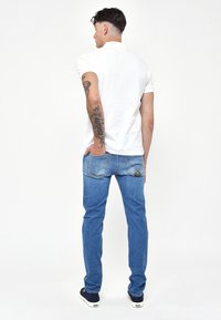 Polo bianco, jeans in denim blu e sneakers nere. I jeans hanno tasche posteriori con dettagli ricamati e una vestibilità slim.