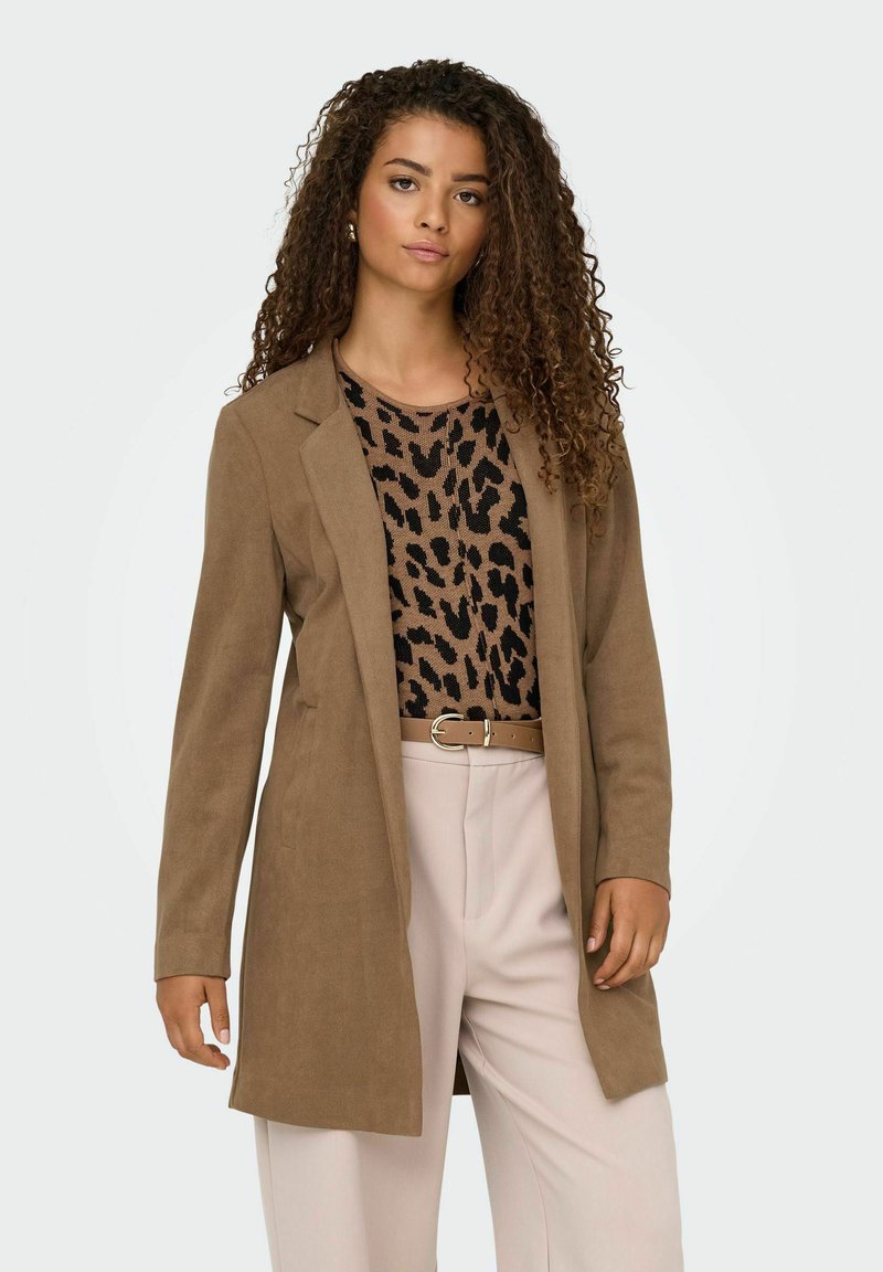 Blazer de ante marrón con mangas largas, solapas con muesca y un corte relajado, combinado con una blusa de estampado de leopardo y pantalones claros.