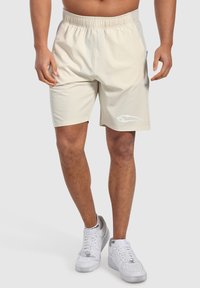 Ljusbeige sportshorts med elastisk midja, sidofickor och en vit logga på vänster ben. Slätt, lättviktigt material.