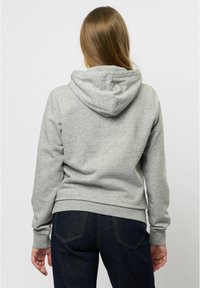 Grå bomullshuvtröja med dragsko, elastiska ärmslut och en åtsittande nederkant. Bärs över mörka denimjeans. Minimalistisk design med en slät textur.